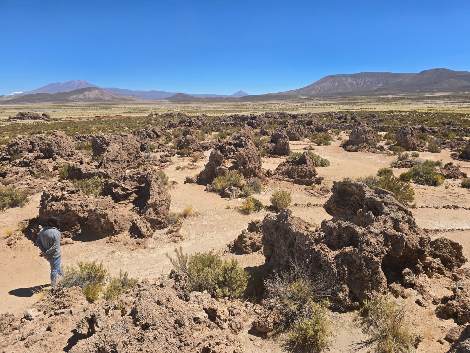 Visitor walking among stone ruins at Kausay Wasi, Andes mountains in background